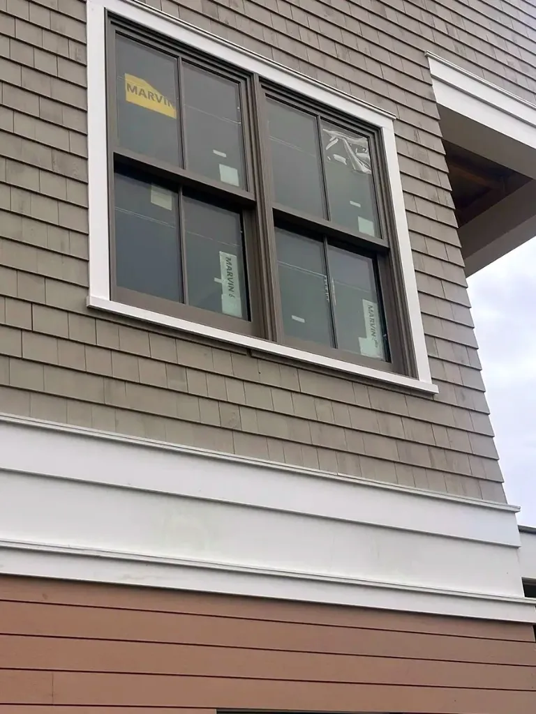 Close-up of cedar shake and lap siding with white trim around a Marvin window