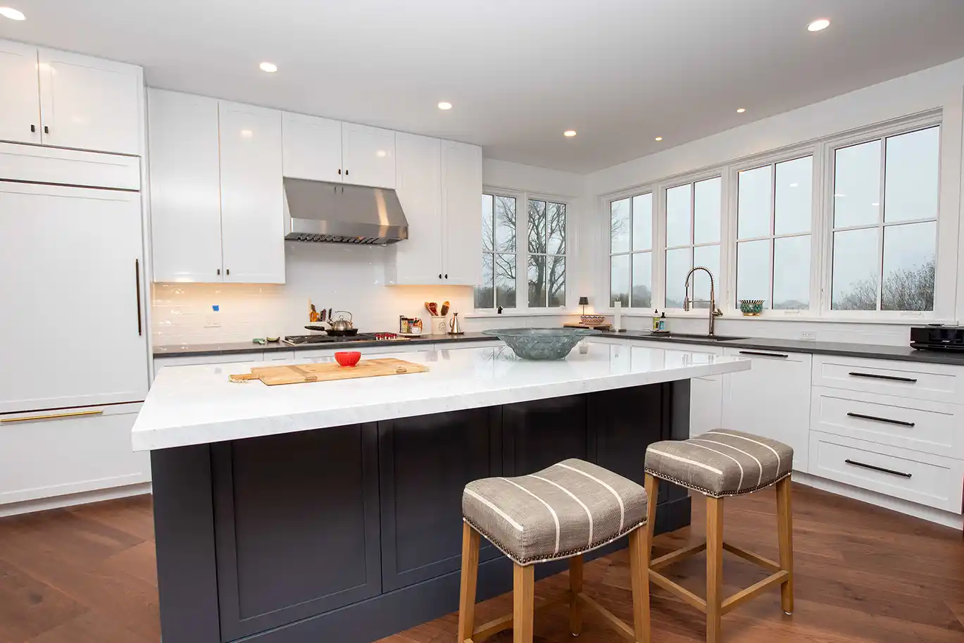 Kitchen with white shaker cabinets, a navy island with stools and windows on two walls