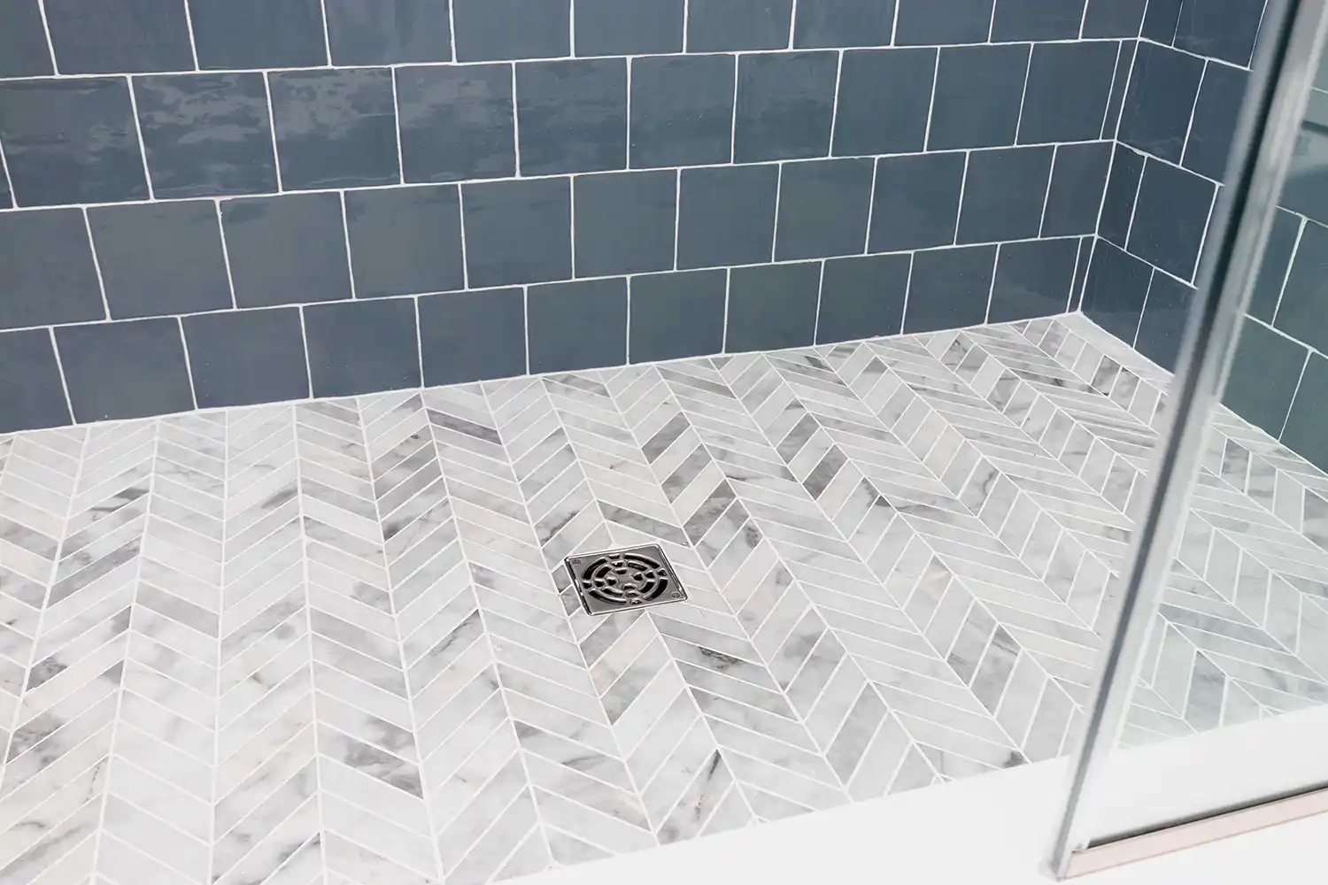 Shower with blue-gray tile walls and a marble herringbone floor pan